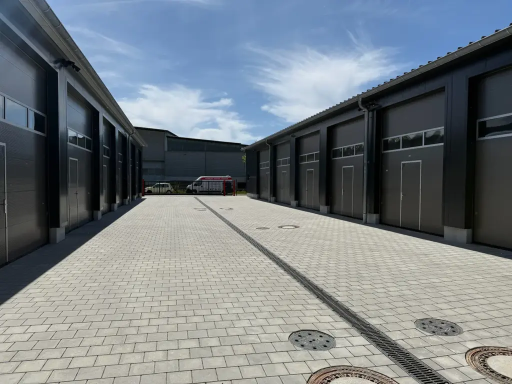 Breiter gepflasterter Zufahrtsbereich zwischen zwei Reihen moderner Lagerhallen in Mering